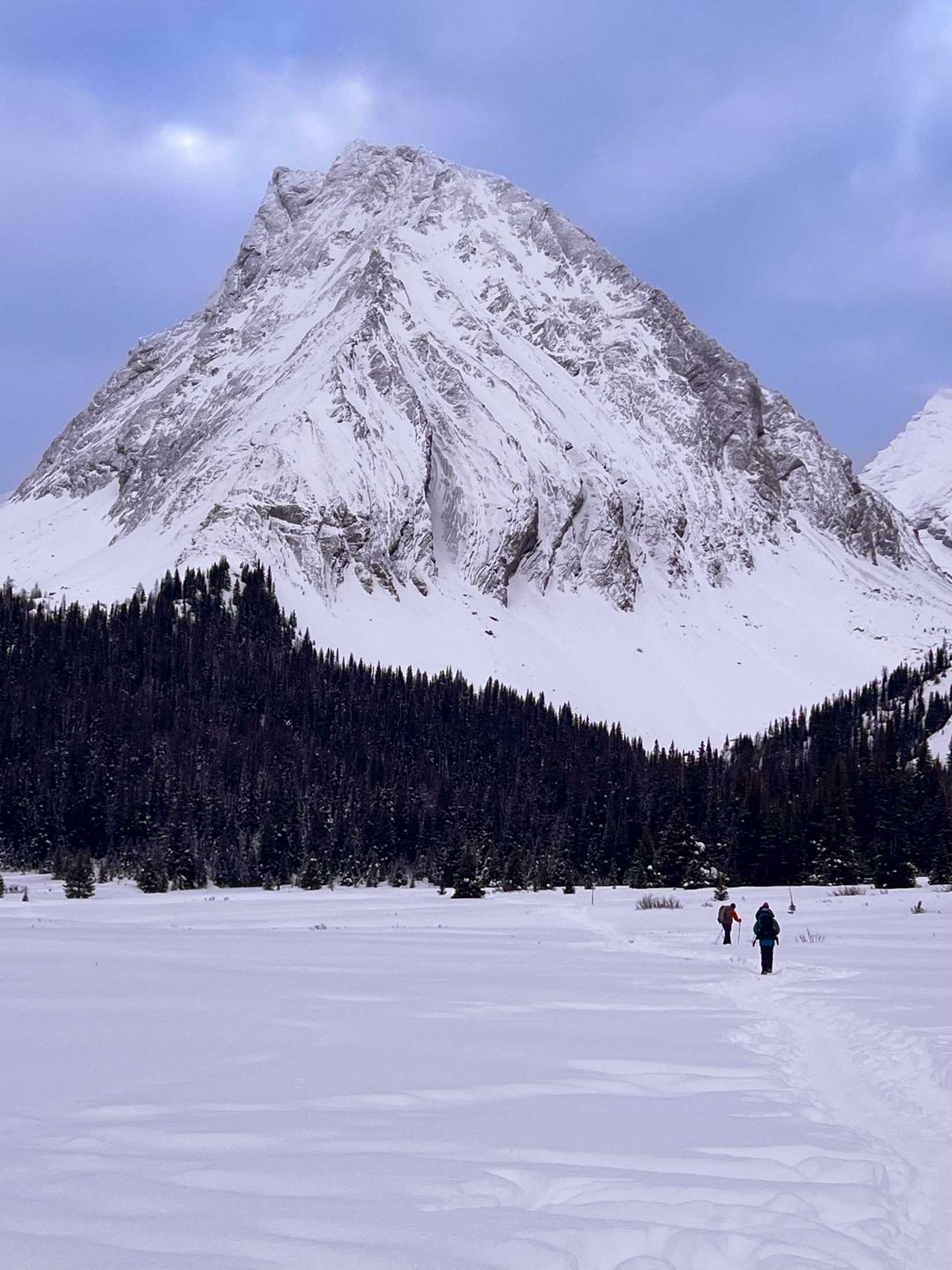 Two hikers crossing a frozen lake beneath a towering peak, Banff