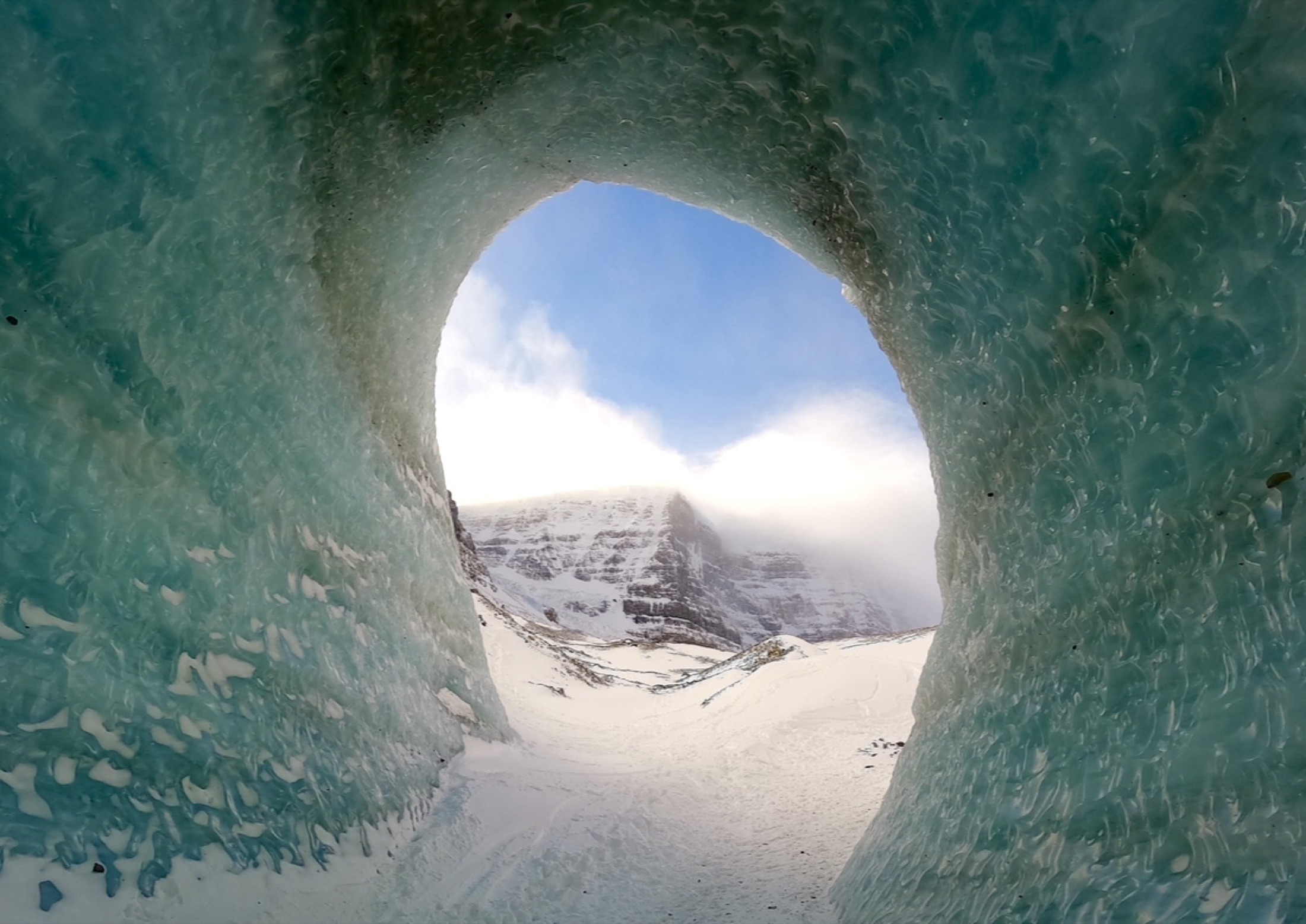 Looking through a teal glacier ice tunnel toward the mountains, Banff