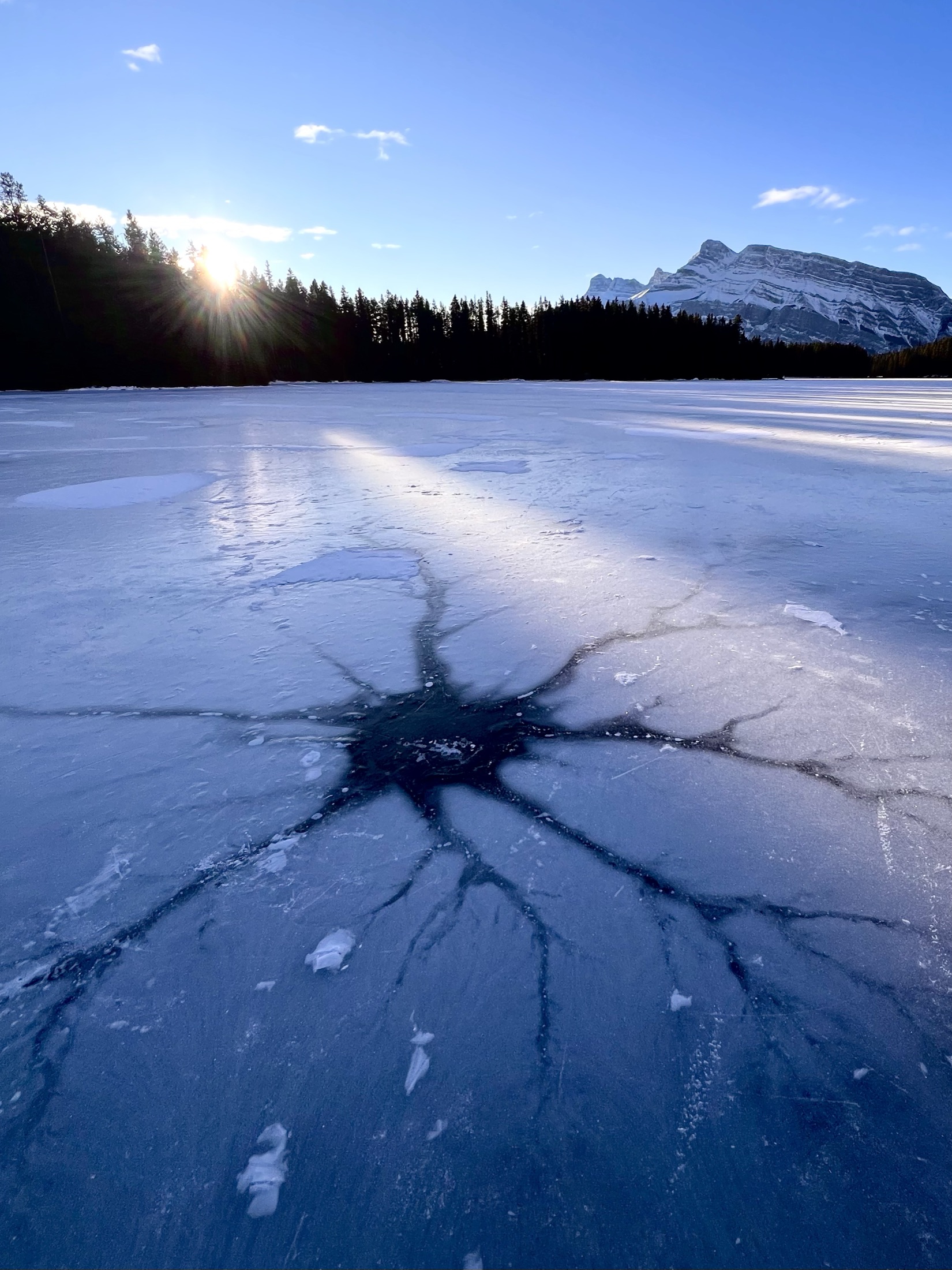 A star-shaped crack pattern in frozen lake ice at sunset, Banff