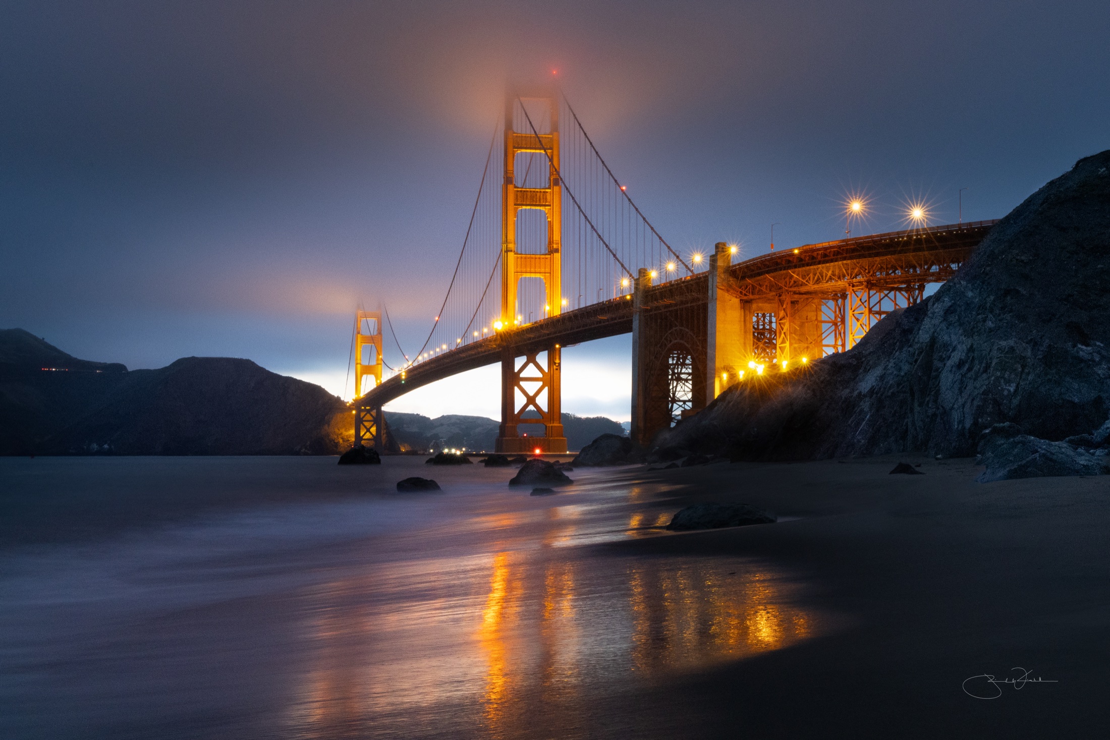 The Golden Gate Bridge at night, fog rolling over the towers